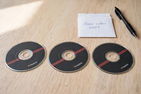 Three 8 cm mini DVD discs with dark printed faces beside a paper sleeve marked Home videos 2007