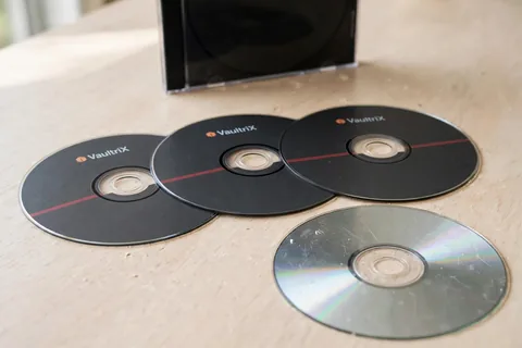 Three dark printed recordable discs and one scratched silver disc beside a black jewel case