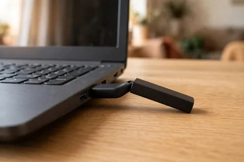 A matte black USB flash drive bent at the neck while seated in a laptop USB port, its body pointing away from the laptop