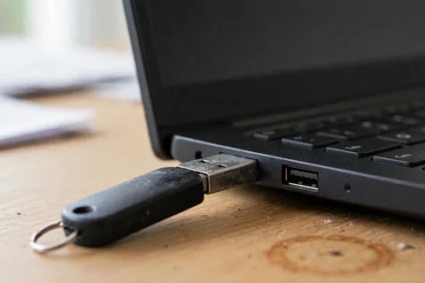 A well-used flash drive with its plug only partly pushed into a laptop USB port, a gap of scratched bare metal showing and the drive hanging loose